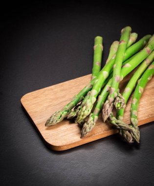 Siyah arka planda ahşap bir tahtada yeşil taze kuşkonmaz. C