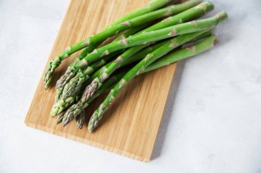 Beyaz arka planda ahşap bir tahtada yeşil taze kuşkonmaz. C