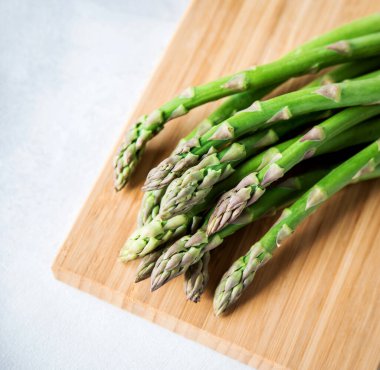 Beyaz arka planda ahşap bir tahtada yeşil taze kuşkonmaz. C