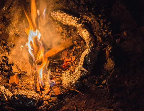 Tin Foil wrapped potatoes cooking by the side of bonfire during camping. Long exposure shot of fire