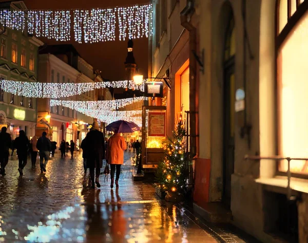 Yağmurlu bir Noel kenti tatil caddesi İnsanlar şemsiyeyle aydınlatılmış dekorasyon ve asfalt Tallinn Estonya 'da yeşil ağaç ışığı yansıması altında yürür Avrupa' ya seyahat yaşam tarzı 