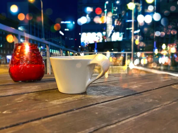 night street cafe table with white cup of coffee and red glass candle at evening city blurred light on buildings windows Tallinn Estonia travel  Europe