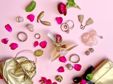 Kadınlar parfüm parfümü ve kırmızı güller çiçek yaprağı, altın kostüm mücevherleri, kozmetik kutular, pembe arka planda küpeler.