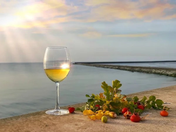 Autumn  grape wine sunset at sea glass of wine with sunshine flare and Autumn leaves yellow with rose hip red berry still life on stone blue sky pink clouds ,, nature landscape seascape skyline