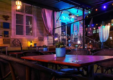 Neon klasik sokak restoranı, masanın üstünde bir bardak şarap ve fincan çiçeği, Tallinn 'deki eski kasabada gece bulanık ışık.