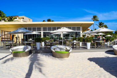 Palmiye ağaçları, beyaz plaj şemsiyeleri ve güneşli bir günde birkaç bulutla Aruba 'nın doğu yakasındaki Eagle Beach' in romantik Bucuti & Tara Resort 'unun nefes kesici manzarası.