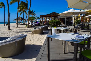 Palmiye ağaçları, beyaz plaj şemsiyeleri ve güneşli bir günde birkaç bulutla Aruba 'nın doğu yakasındaki Eagle Beach' in romantik Bucuti & Tara Resort 'unun nefes kesici manzarası.