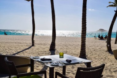 Palmiye ağaçları, beyaz plaj şemsiyeleri ve güneşli bir günde birkaç bulutla Aruba 'nın doğu yakasındaki Eagle Beach' in romantik Bucuti & Tara Resort 'unun nefes kesici manzarası.