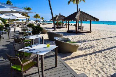 Palmiye ağaçları, beyaz plaj şemsiyeleri ve güneşli bir günde birkaç bulutla Aruba 'nın doğu yakasındaki Eagle Beach' in romantik Bucuti & Tara Resort 'unun nefes kesici manzarası.