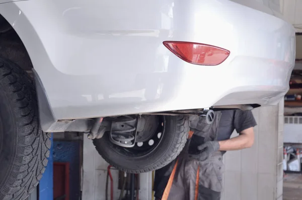 Car on a lift, in service center for maintenance , technician inspecting.