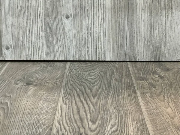 Perspective of light beige wood in front of a gray wooden background.