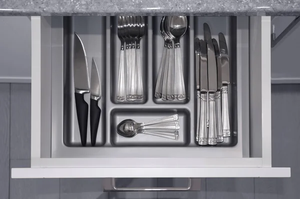 Grey opened kitchen drawer with a tray and silvery cutlery set with spoons, knife and fork inside. View from above. Image