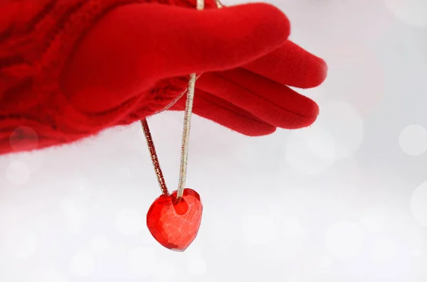 Hand in a red glove and red heart with a gold rope on a light background. St. Valentine\'s Day background. Empty place for text. Image