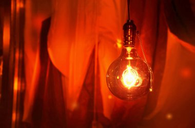 Ampul arka plan kırmızı perdeler üzerinde sıcak ışık renkte yanıyor. Metin için boş yer. IMAG