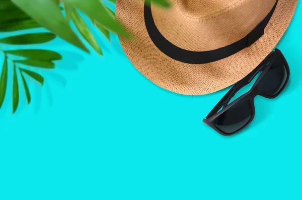 Turquoise background with sunglasses, hat, camera and palm leave