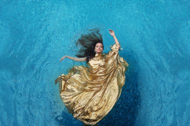 beautiful young woman in gold dress, evening dress floating weightlessly elegant floating in the water in the pool dark brown hair drift fan-shaped in turquoise water clipart