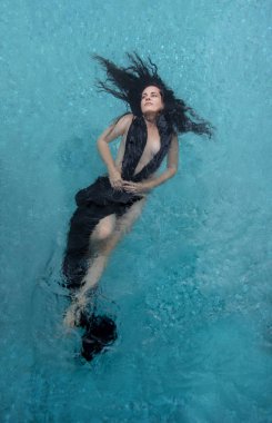 beautiful woman with dark curly hair in black dress, evening dress floats elegantly floating happy in turquoise blue water in the pool clipart