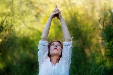 Kızıl saçlı Bayan spor giyim güneşin doğada doğada Yoga egzersizleri elle yapıyor
