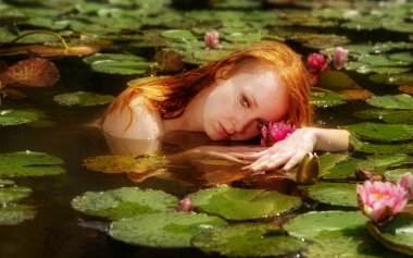ihale genç seksi redhead kadın Ophelia seductively sensually yüzen su, göl, gölet, marsh ve pembe nilüferler ile oynuyor.