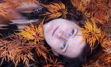 Güzel genç bireysel, eksantrik ve kadın ile ilginç saç modeli, dreadlocks, piercing dövme, renkli sonbahar akçaağaç yaprakları tarafından kapalı Bahçe cennet yatıyor