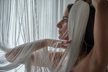 Güzel bir genç çekici kadın, çıplak seksi, kısmen bir dize perde beyaz iş parçacıkları tarafından gizli profil portresi dans gibi ellerini hareket eder.