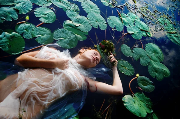 Beyaz elbiseli göl suda ölmekten Kapalı gözlerle çiçekler olan genç seksi kadın Ophelia kıvırcık kırmızı saçlı yatıyor