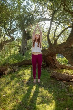 Kızıl saçlı Bayan spor giyim güneşin doğada doğada Yoga egzersizleri elle yapıyor