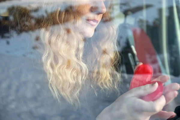 Nose and mouth of a portrait of a young sexy woman with blond curly hair sitting thoughtfully in the car and warming her hands on a heart shaped pocket warmer. — Stock Photo, Image