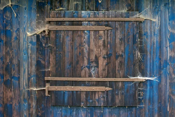 Eine rustikale Holzschuppenwand aus blauem Brett mit verschlossenem Fenster mit rustikaler Holzmaserung und vielen Spinnennetzen — Stockfoto