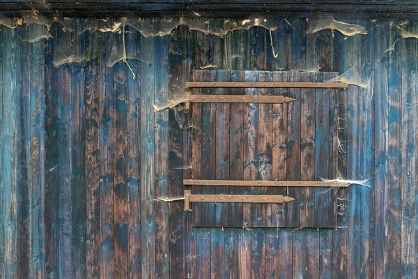 Schöne grunge blaue Holzbrettwand eines alten Schuppens mit verschlossenem Fenster mit Holzmaserung und vielen Spinnennetzen — Stockfoto
