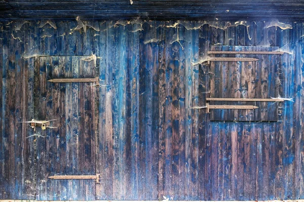 Blaue Holzbrettwand eines Schuppens mit verschlossenen Fenstern und verschlossener Tür mit Holzmaserung und vielen Spinnennetzen — Stockfoto