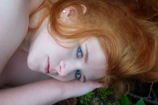 Hermoso retrato de una joven acostada encantadora chica con el pelo rojo y los ojos azules en el musgo — Foto de Stock