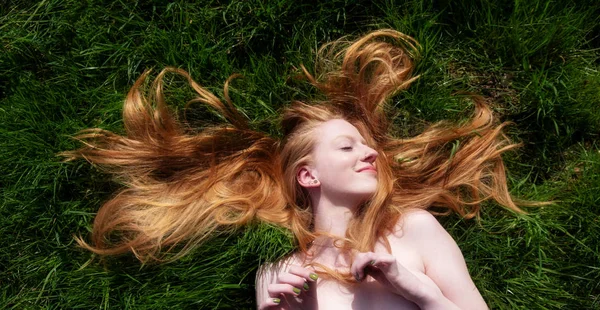 Retrato de una hermosa joven sexy pelirroja, acostada en el verano bajo el sol en la felicidad, acostada sobre la hierba verde, el pelo rojo envuelto libremente alrededor de la cabeza . — Foto de Stock