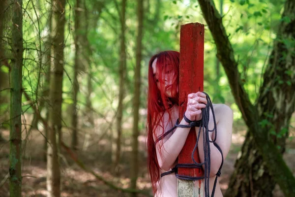 Young sexy naked woman with red hair is tied to a post with a rope — Stock Photo, Image