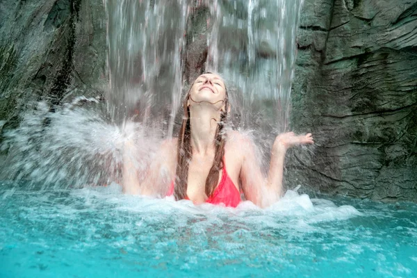 Joven mujer rubia sexy en bikini fucsia levanta las manos contra las salpicaduras de agua de la cascada —  Fotos de Stock