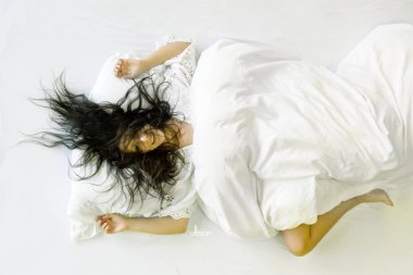 Çekici, genç, seksi, koyu saçlı kadın, çarşaf üzerinde saç vahşi, ağız açık, gülerek, metin için boş alan ile yatakta yalan.