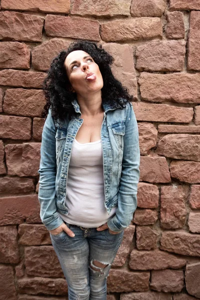 naughty curly dark haired woman with denim jacket is sticking out tongue