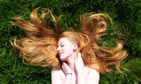 Ritratto di una bella giovane donna dai capelli rossi sexy, sdraiata sotto il sole primaverile che si rilassa sull'erba verde, i capelli rossi si avvolgono liberamente intorno alla testa . — Foto Stock