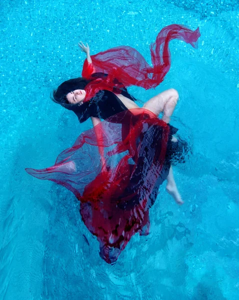 Bela jovem mulher relaxada em vestido preto e vermelho alegremente flutuando na água na piscina — Fotografia de Stock