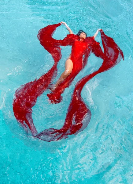 Belle jeune femme avec la maladie de vitiligo en robe rouge, robe de soirée flottant en apesanteur élégant dans l'eau dans la piscine — Photo