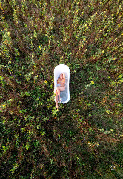 View from above of a young beautiful woman,, takes a bath in a bathtub in nature in the sunset between sunflowers