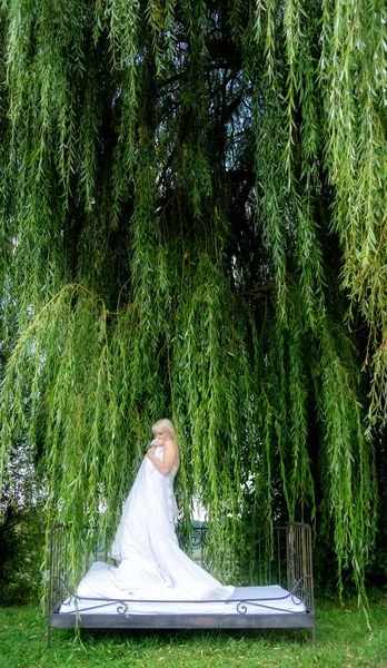 Přitažlivá, mladá, sexy blondýnka stojící s bílým duvesem v posteli, v přírodě pod plačící vrbovou větví — Stock fotografie