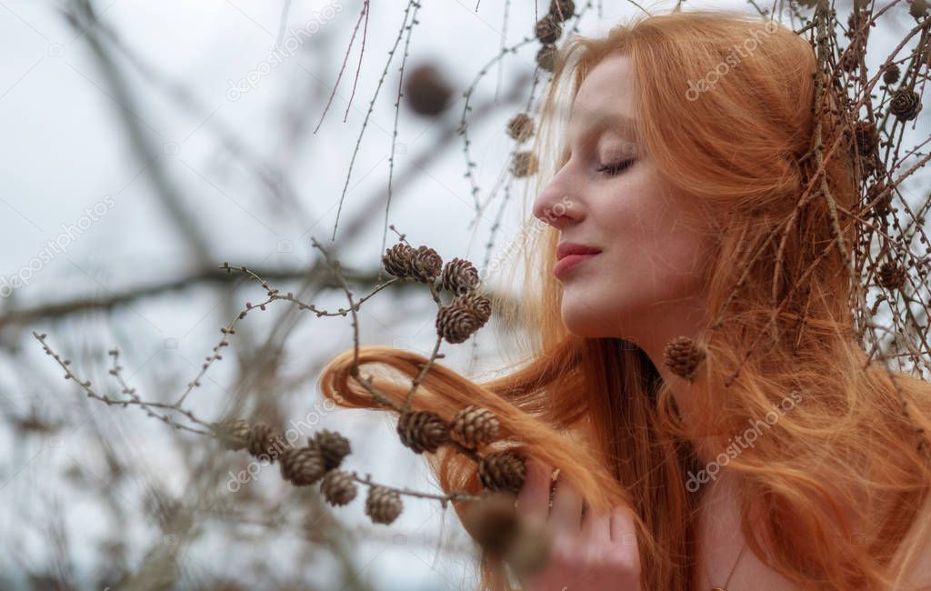 young beautiful sexy redhead woman plays smiling with pine cones and her beautiful red hair caught in a pine branch.