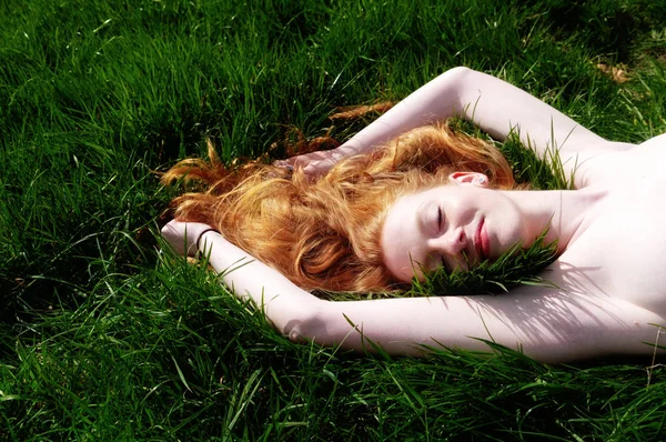 Genç ve seksi kızıl saçlı bir kadının güzel portresi, kollarını kaldırıyor, yeşil çimlerin üzerinde yaz güneşinde yatıyor, kızıl saçlar özgürce başının etrafına sarılmış.. — Stok fotoğraf