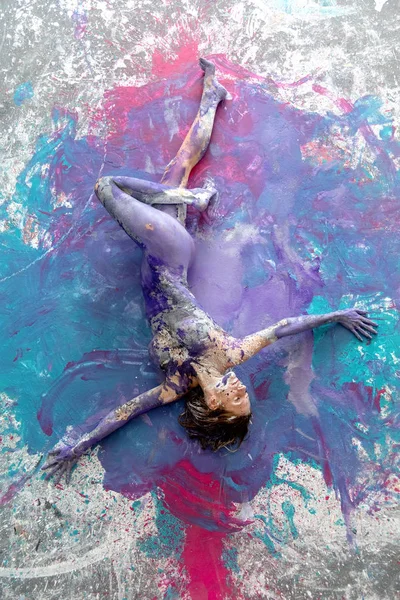 Junge nackte Frau in rosa, türkis, lila, farbig bemalt, liegt dekorativ und tanzt elegant auf dem Boden. kreative, abstrakte Körperkunst und Malerei. — Stockfoto