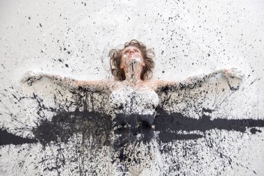 Portrait and arms of artistically abstract painted woman in black and white paint on the floor in studio. Creative expressive body painting art.