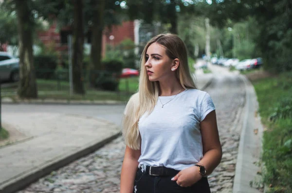 Yeşil sokak arka plan üzerinde beyaz bir t-shirt duran güzel sarışın.