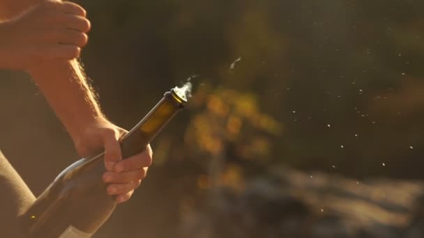 El hombre abre la botella de champán. Explosión de champán. Champán estallando. Vino espumoso al atardecer salida del sol al aire libre. El hombre sacude una botella salpicando champán — Vídeo de stock