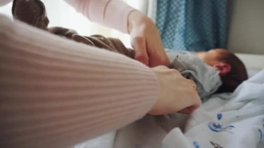 Yeni doğmuş bir bebek pencerenin yanındaki soyunma masasında yatıyor. Annem bebek pantolonunu giyer. Küçük bir çocuğa bakmak. Anne ve oğul.