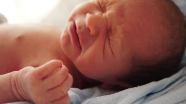 Yeni doğmuş bir bebeğin portresi mavi bir yatak örtüsünün üzerinde uzanıyor ve hapşırıyor. Kıyafetsiz. Hayatın ilk anları. Yeni doğan bebek yüz portresinin yakın çekimi